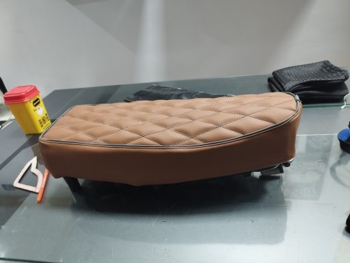 Funda de asiento marrón con diseño acolchado sobre una superficie de vidrio.