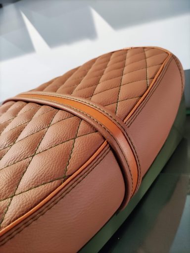 Bolso de cuero marrón con diseño acolchado y detalles en naranja.