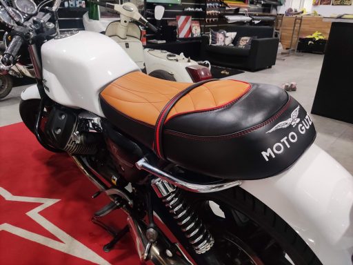 Asiento de motocicleta con tapizado naranja y negro en un entorno de taller.