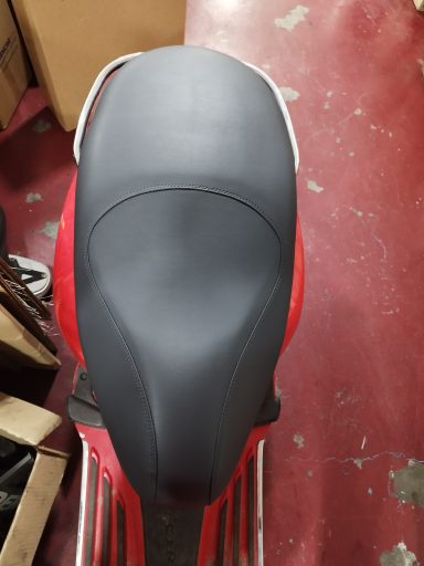 Asiento negro de una moto, visto desde arriba, sobre un fondo de suelo rojo.