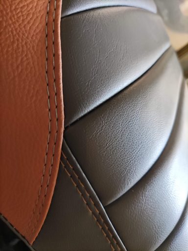 Textura de un asiento de cuero en tonos negro y marrón, con costuras visibles.