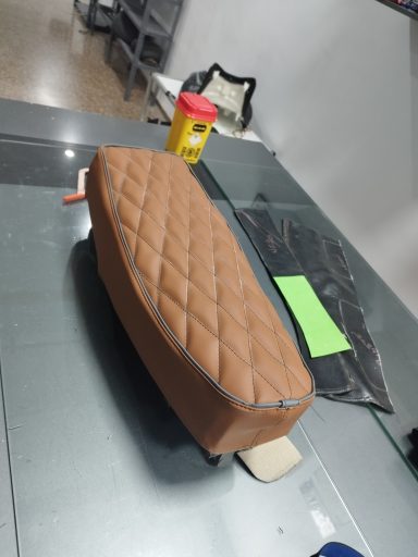 Cojín marrón con diseño de rombos, sobre una mesa de metal.