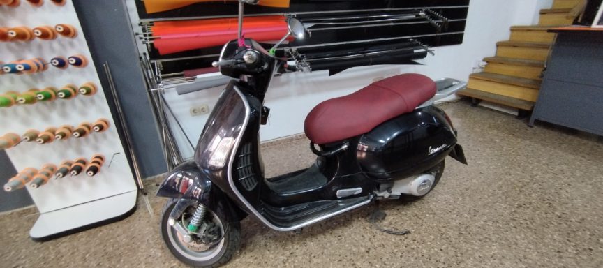 Scooter negro con asiento burdeos, estacionado en un interior comercial.
