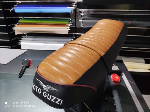 Asiento de moto de color marrón con detalles negros y logotipo de Moto Guzzi.