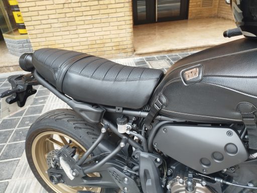 Asiento de motocicleta negro con costuras, parte lateral de la moto visible.