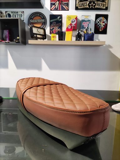 Sillín de moto marrón con diseño acolchado y base negra sobre una mesa.