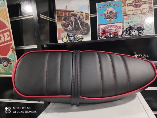 Asiento de motocicleta negro con costuras rojas, decorado con carteles retro de motos.