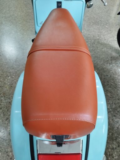 Asiento de moto de color marrón sobre un fondo azul claro, con textura suave.